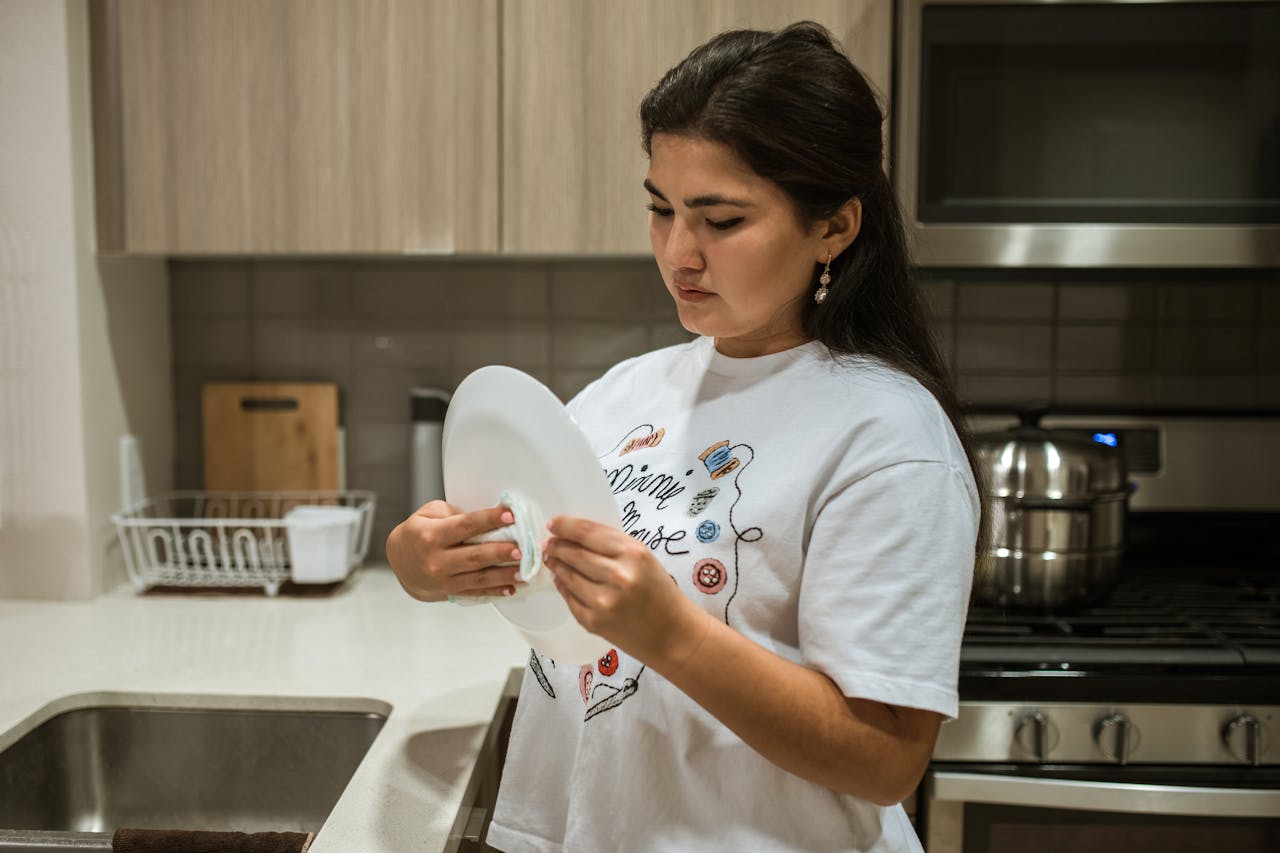 about-us Woman attentively wiping a plate in a contemporary kitchen setting.