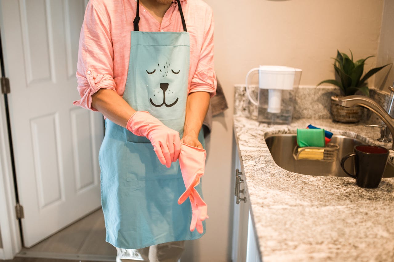 services-05 Person in a kitchen putting on rubber gloves with a cute animal-themed apron. Indoor setting.